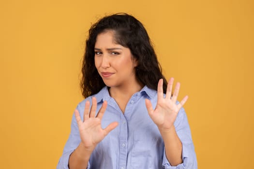 Skeptical young woman in a blue shirt, showing her palms in a defensive stop