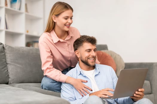 Millennial couple using laptop watching movie comfortably sitting at home