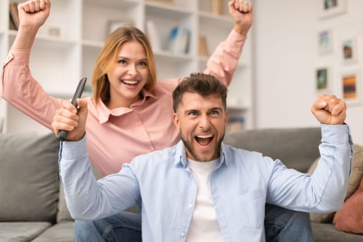 Excited Couple Watching TV And Shaking Fists In Joy Indoors