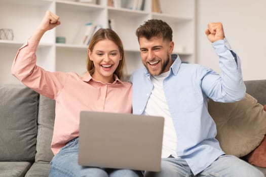 Young spouses celebrate victory on their laptop in living room