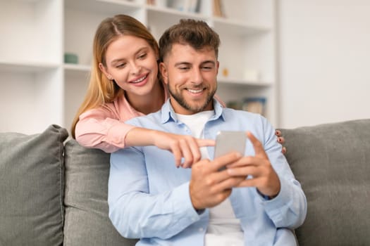 Millennial couple engrossed in smartphone browsing social media at home
