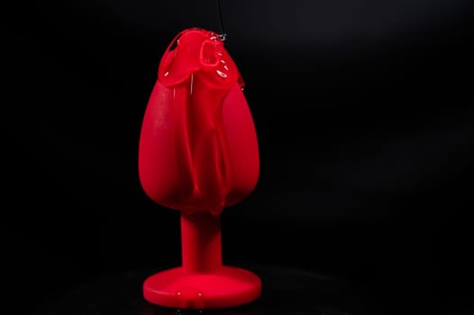Intimate lubricant pours on a red anal plug on a black background. Copy space.