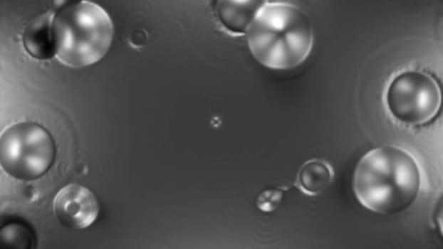Boiling unknown liquid substance. Design. Round spherical bubbles appear on calm surface.