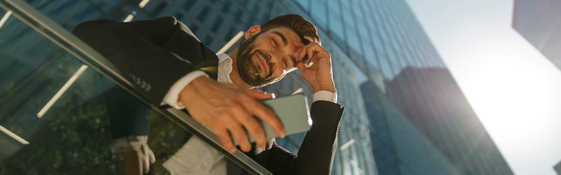 Bottom view of handsome businessman using mobile phone standing on background of skyscrapers