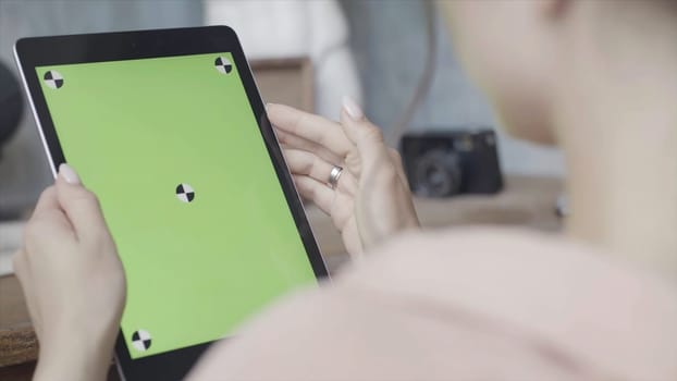 Side view of a woman holding tablet pc with green screen on wooden table background. Stock footage. Close up of a girl using Ipad with chroma key.