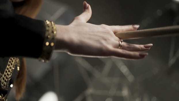 Young attractive woman hand holding drumstick and rotating it during musical rehearsal. Action. Close up for woman hand with manicure and gold rings holding and spinning a drumstick.