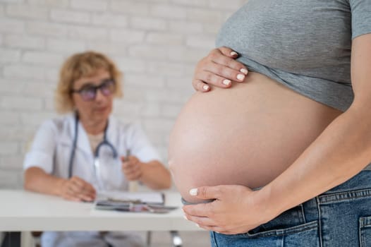 Doctor obstetrician gynecologist at his desk in the background. Close-up of a pregnant woman's belly.