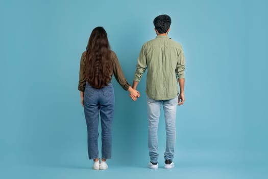 Back view of millennial couple posing on blue background