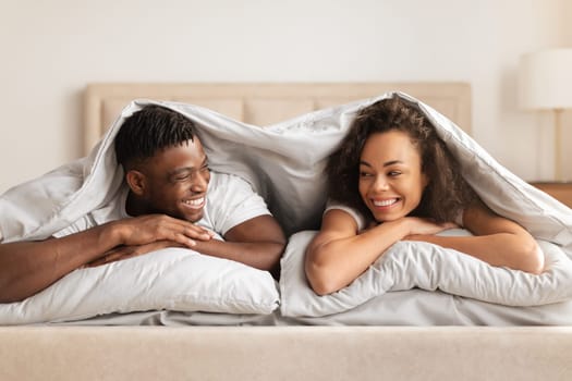 Young African American Couple Lying Under Blanket In Bedroom