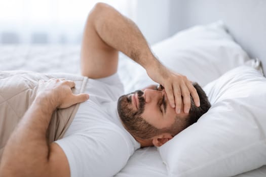Man awake in bed suffering from headache touching forehead indoors