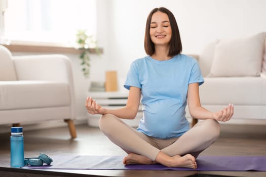 Smiling calm pregnant woman in casual practicing prenatal yoga indoor