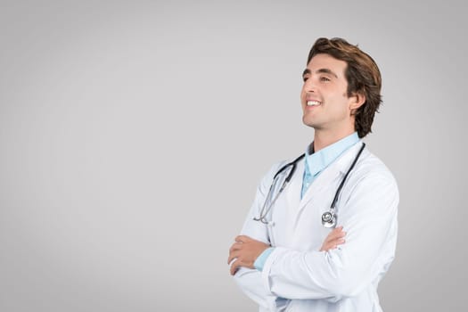 Confident male doctor looking aside posing near empty space for medical advertisement text or design, grey background