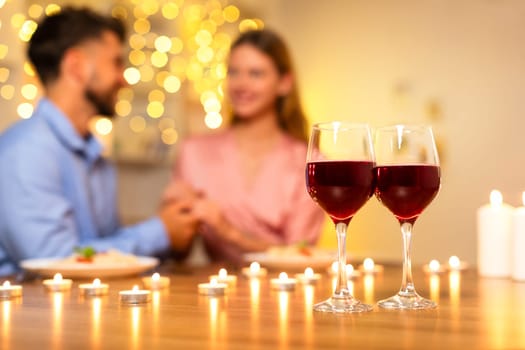 Couple in blurred background holding hands, wine glasses focused in front