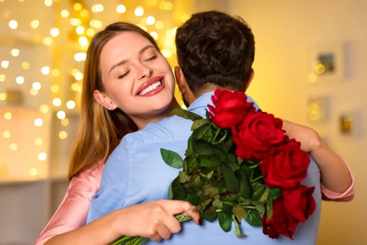 Joyful woman embracing man, holding red roses with festive lights