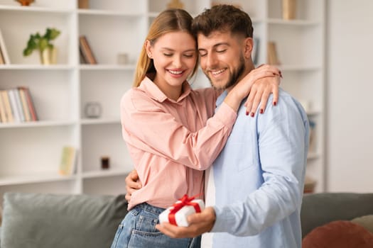 Smiling husband presenting wrapped gift box to wife at home
