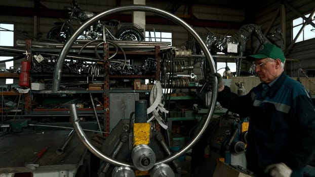 Metalworking machine for bending industrial steel tubes. Creative. Worker in uniform making a detail in a form of hoop with the workshop on the background.