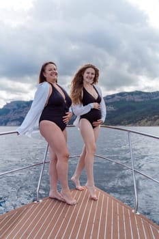 Pregnant on a yacht. Happy models in a swimsuit posing on a yacht against sky with clouds and mountains.