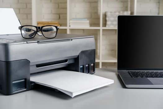 Printer and laptop on grey table in office