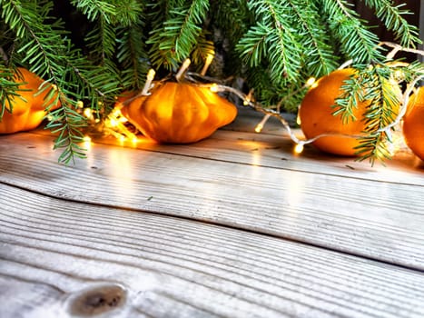 Festive decoration with bouquet and branches of spruce, bright glowing garlands, oranges on wooden background. Decor for Christmas and New Year. Abstract texture, frame, place for text, copy space