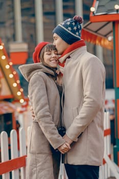 Romantic couple sharing a kiss at a vibrant Christmas fair with festive decorations