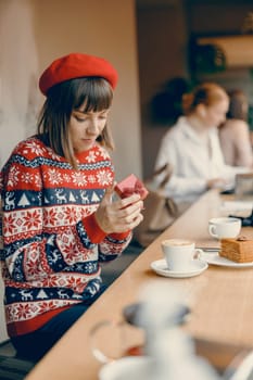 A thoughtful woman in a holiday sweater gently unwraps a gift,immersed in the festive spirit of a warm and inviting cafe