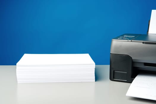Laser printer on desk against blue background.
