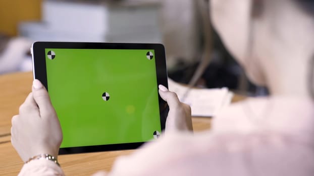 Rear view of a brunette woman using tablet with green screen, modern technologies concept. Stock footage. Female holding ipad with chromakey and reading something.