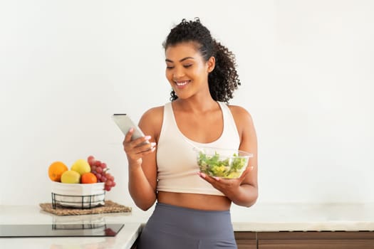 fitness lady browsing recipes on smartphone eating nutritious salad indoor