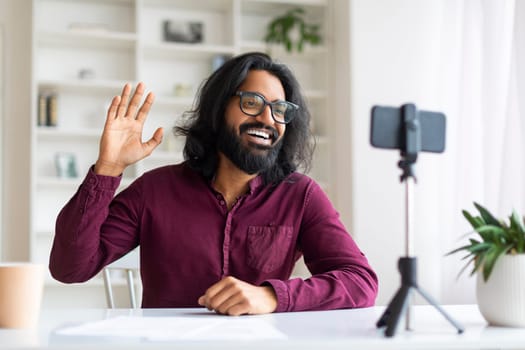 Cheerful Indian freelancer guy waving hello during live stream or video call