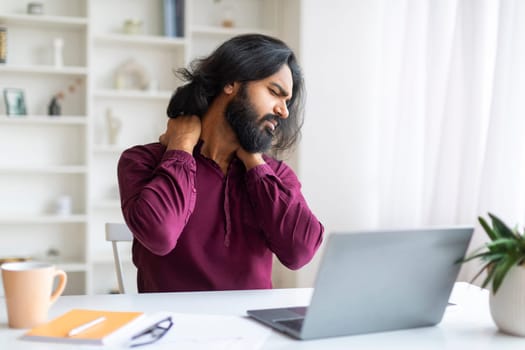 Tired Indian Freelancer Man With Neck Pain Sitting At Desk With Laptop