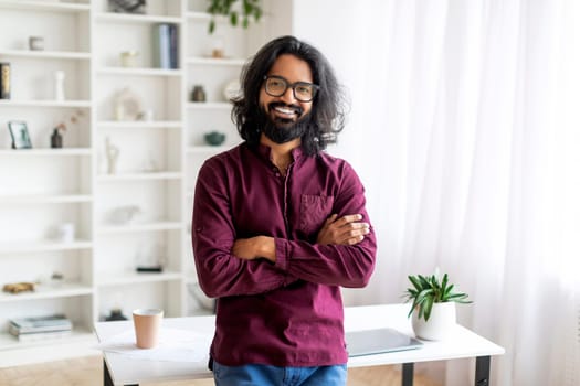 Smiling Indian Man Standing With Folded Arms Near Desk At Home Office