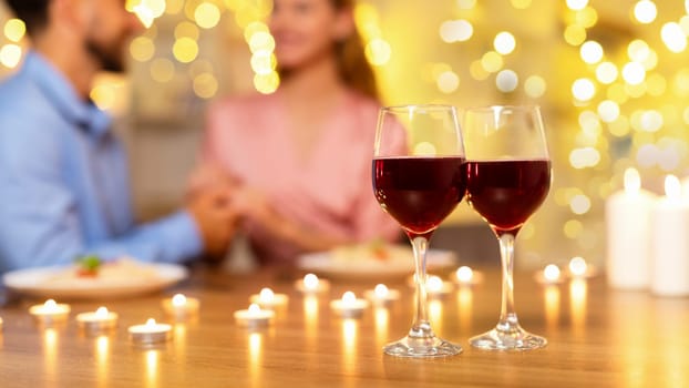 Close-up of wine glasses with couple and candles in the background