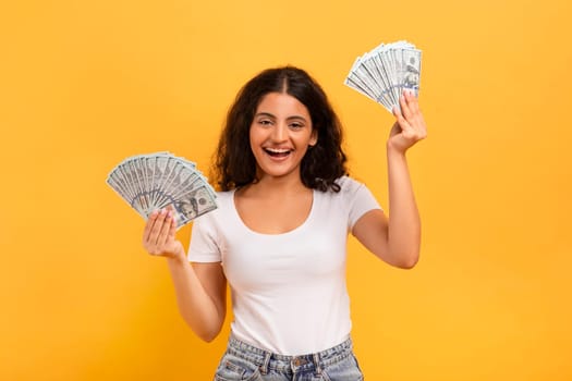 Excited young indian woman holding bunch of money banknotes