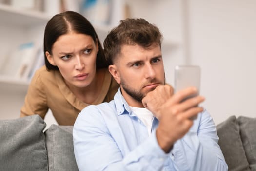 Distrustful young woman sneakily checks her boyfriend's phone at home