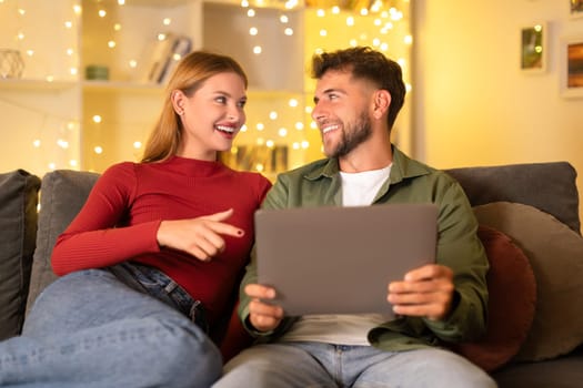 Engaged couple sharing a tablet with cozy lights in the background