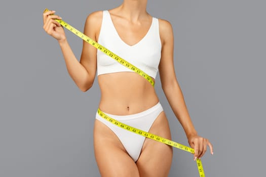 Young european lady in white sportswear use yellow measuring tape around body to highlight fitness progress