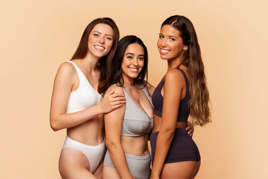 Three cheerful multiracial women in underwear embrace and smile