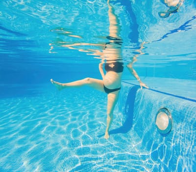 Embracing aquatic fitness, a pregnant woman demonstrates strength and serenity in underwater aerobics, creating a serene and empowering image in the pool