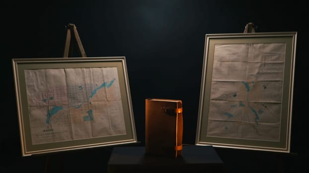 Exposition of old leather bound notebook between two old maps standing in te dark room. Stock footage. Museum exhibition