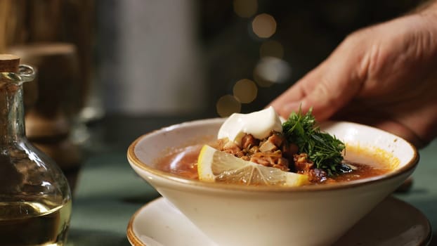 Close-up of hand taking the plate with Russian traditional soup solyanka from the table. Stock footage. Russian solyanka soup with meat, sausages and olives