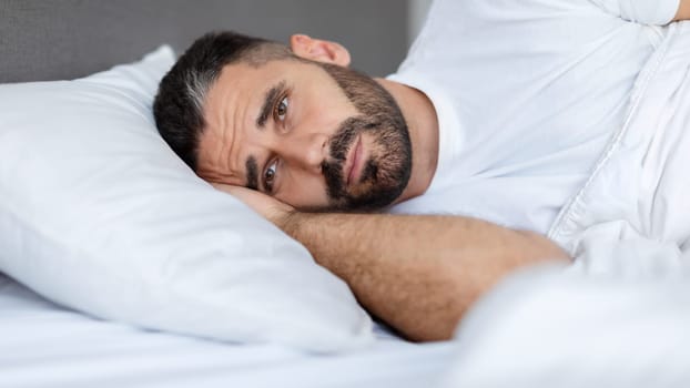European man lying awake having insomnia problem in bed indoor
