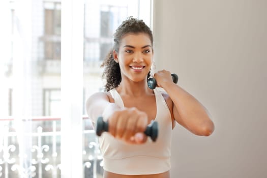 athletic woman holds dumbbells exercising with smile in living room