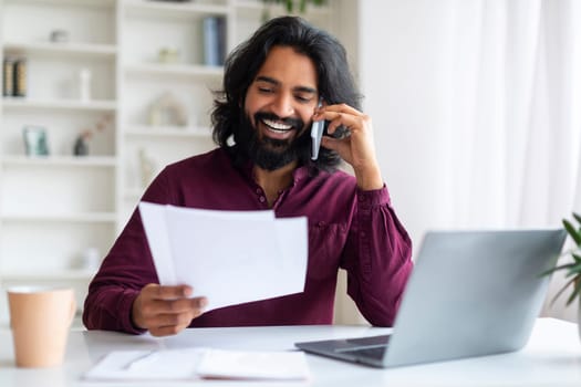 Busy Indian Freelancer Guy Checking Papers And Talking On Cellphone At Home