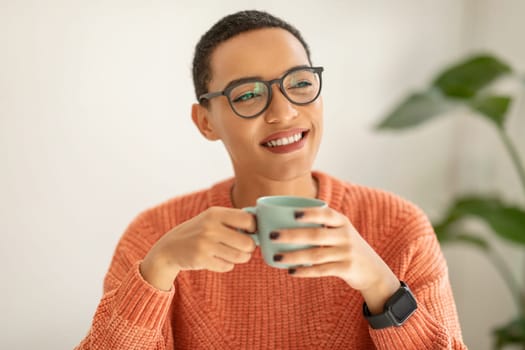 Smiling pretty millennial latin woman in glasses enjoy peace and spare time, drink cup of coffee, warm moment in cafe, office interior. Human emotions, lifestyle, rest, create idea