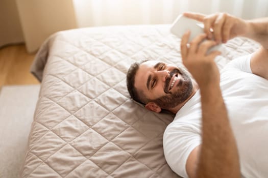 Middle aged guy browsing internet on phone at home bedroom