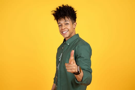 Stylish cool black guy pointing at camera, yellow background