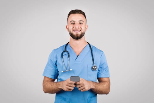 Smiling male nurse in blue scrubs holding a smartphone