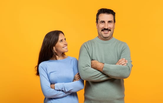 Smiling european old man and woman stand side by side against vibrant orange background