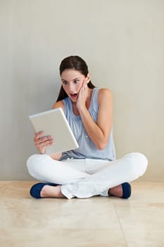 Woman, tablet and surprised on social media, news or gossip sitting against a wall at home. Shocked female person, brunette or freelancer gasping on technology for notification, alert or information.