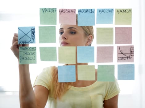 Woman, writing on sticky notes and glass wall with schedule, serious and planning. Copywriter, brainstorming and office job with calendar, workplace and moodboard for ideas, content plan and creative